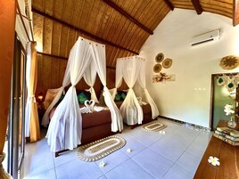 Una habitación con una cama bajo un dosel, techo de madera, aire acondicionado de pared y una pequeña mesa con libros y un jarrón.