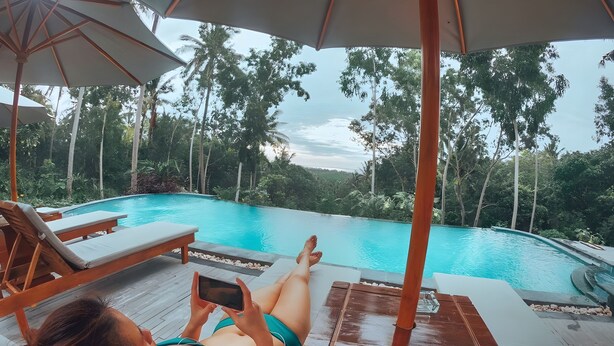 Une femme allongée sur une chaise longue au bord d’une piscine, utilisant une tablette.