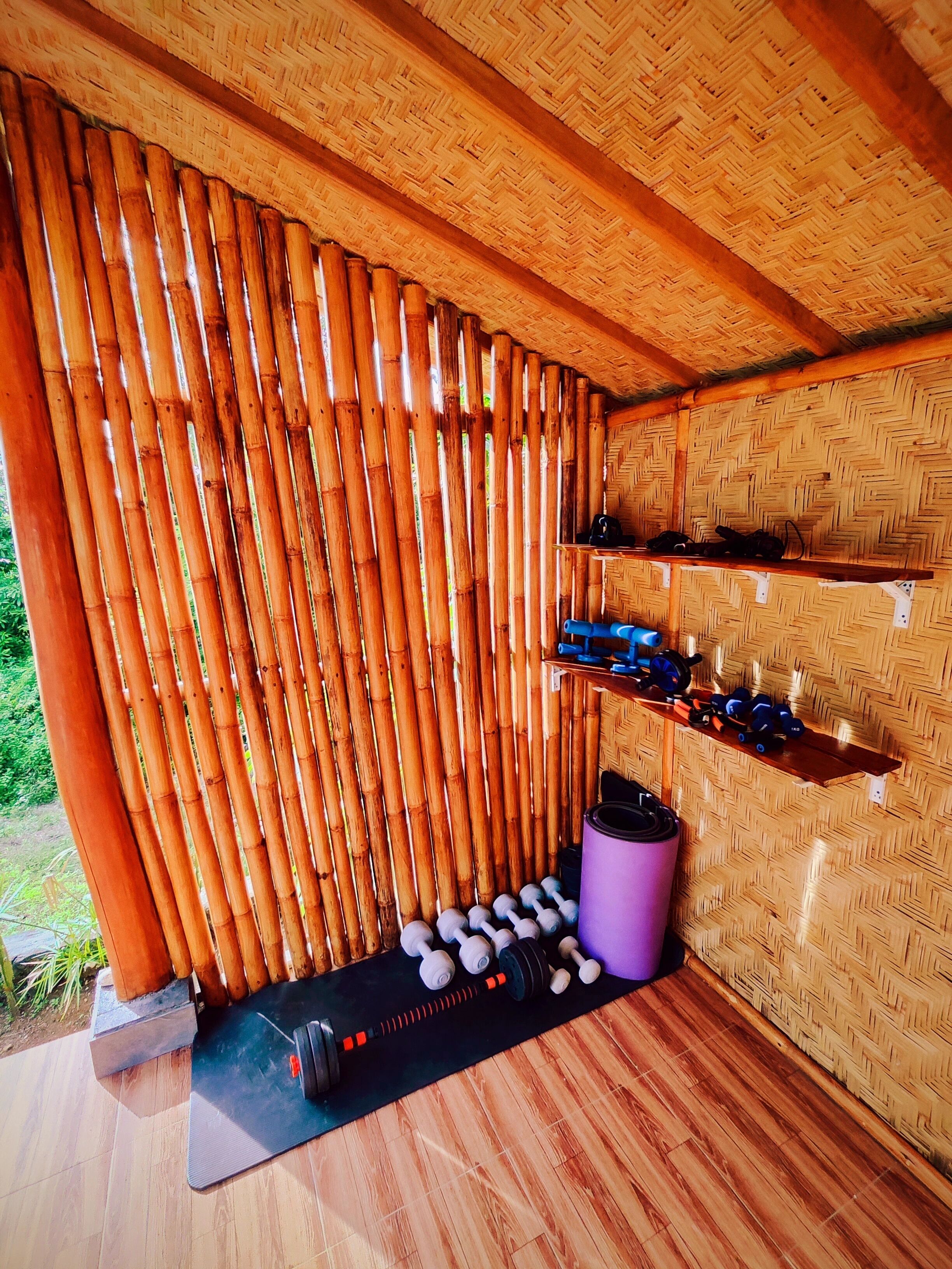 Pared de bambú con estantes que sostienen mancuernas y una colchoneta de yoga.