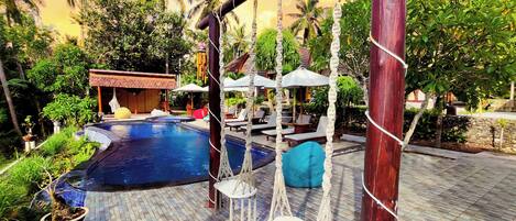 A pool area with a swing chair, lounge chairs, and a small building in the background.