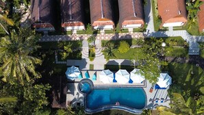 Vue aérienne d’un quartier résidentiel avec une piscine, entouré d’une végétation luxuriante et de maisons aux toits recouverts de tuiles rouges.
