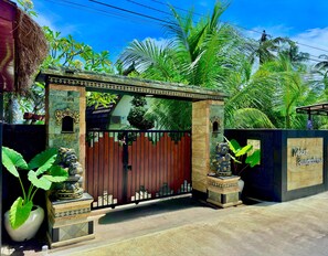 Una entrada cerrada con un portón decorativo, un muro de piedra con un ventanal pequeño y un letrero.