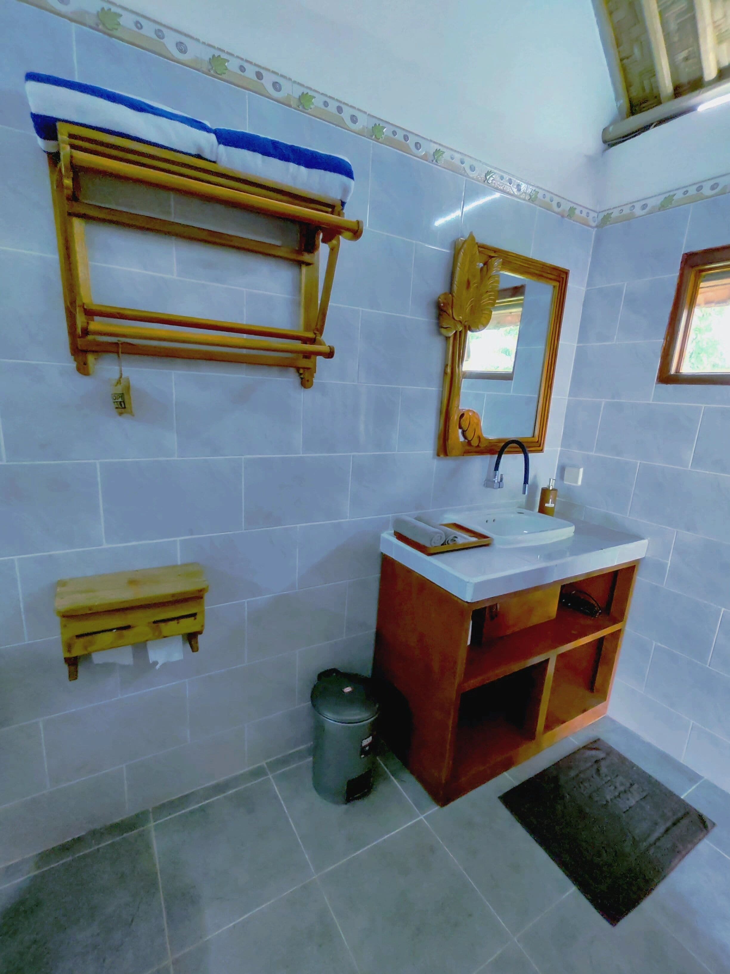 A bathroom with a wooden shelf, a mirror, a sink, and a trash bin.