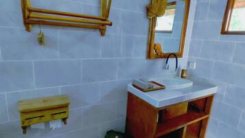 A bathroom with a wooden shelf, a mirror, a sink, and a trash bin.