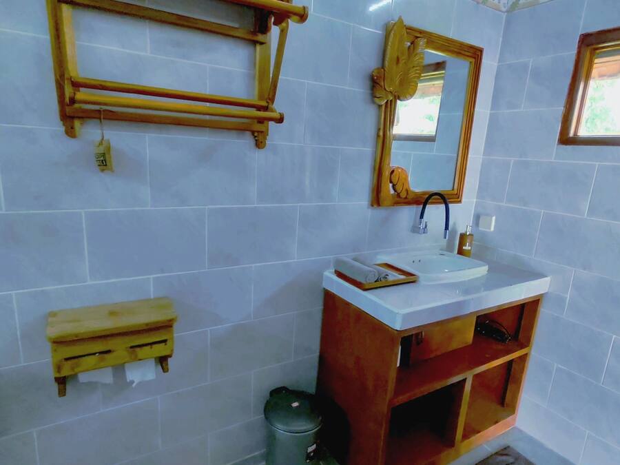 A bathroom with a wooden shelf, a mirror, a sink, and a trash bin.