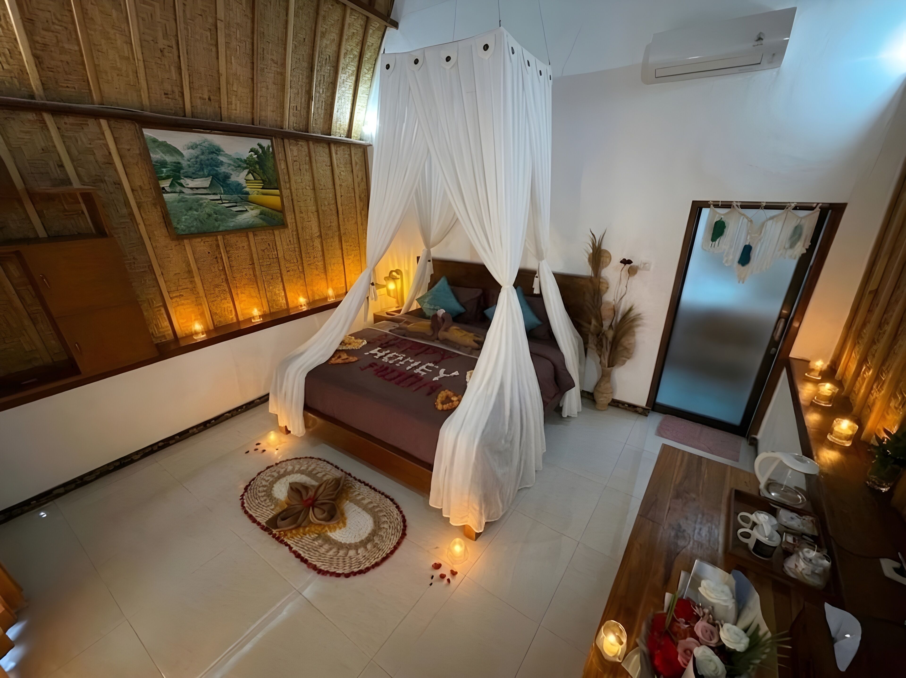 Une chambre à coucher avec un lit sous un dais, une table de chevet avec une lampe, un climatiseur fixé au mur et un miroir.
