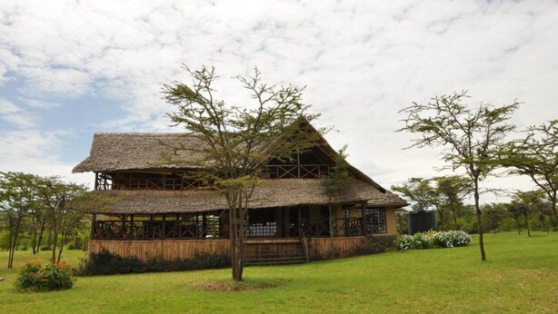 A two-story building with a thatched roof, surrounded by a grassy area and trees. - Ol Loika Cottage (Naivasha)