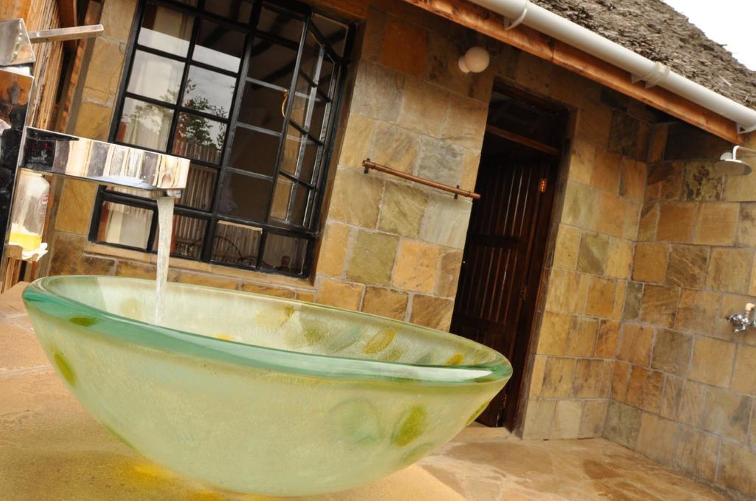 Una grande ciotola di vetro piena d'acqua, posizionata all'aperto di fronte a un edificio in pietra con una finestra e una porta.