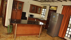 A kitchen with wooden cabinets, a black countertop, a stainless steel refrigerator, and a microwave. - Ol Loika Cottage (Naivasha)
