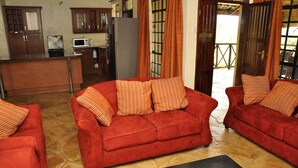 A cozy living area with two red sofas and matching cushions, a black coffee table, and a kitchen in the background. - Ol Loika Cottage (Naivasha)