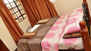 A neatly made bed with floral bedding, a wooden headboard, and a window with curtains. - Ol Loika Cottage (Naivasha)