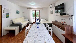 A compact living space with a sofa, a dining table, a kitchenette, and a TV. - Holiday apartment mit Terrasse und Klimaanlage (Šilo)
