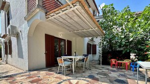A courtyard with a tiled floor, a table with chairs, and colorful plastic chairs. - Holiday apartment mit Terrasse und Klimaanlage (Šilo)
