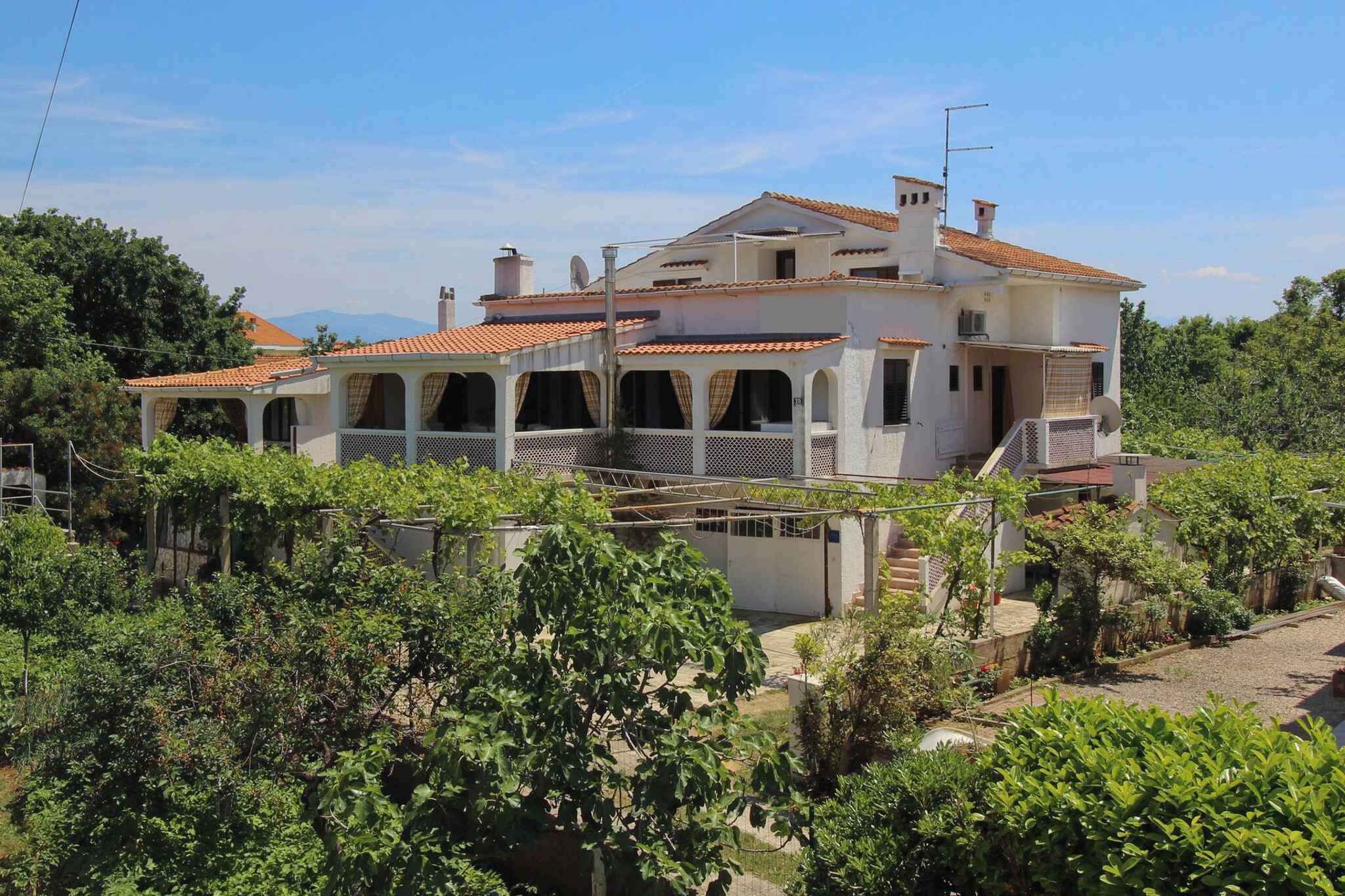 A two-story house with a tiled roof, surrounded by greenery and trees.