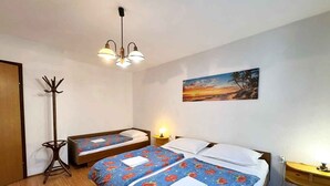 A room with two beds, a coat rack, a painting, and a ceiling light fixture. - Holiday apartment mit Terrasse und Klimaanlage (Šilo)