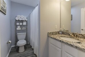 A bathroom with a toilet, a shelf with towels, a sink with a granite countertop, and a mirror. - Western Comfort (Branson)