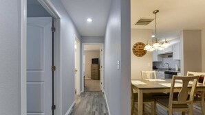 A hallway leading to a dining area with a wooden table and chairs, a kitchen in the background, and a wall clock. - Western Comfort (Branson)