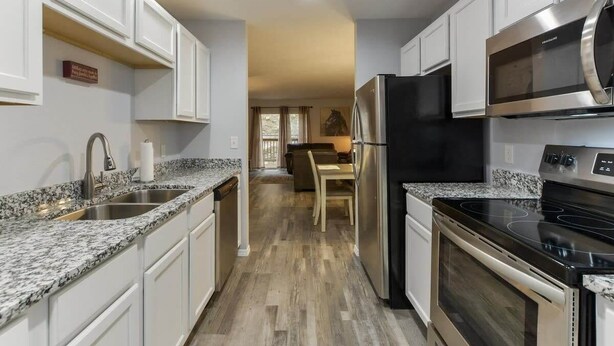 A kitchen with white cabinets, granite countertops, stainless steel appliances, and a wooden floor. - Western Comfort (Branson)