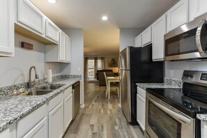 Une cuisine avec des armoires blanches, des comptoirs en granit, des appareils électroménagers en acier inoxydable et un plancher en bois.