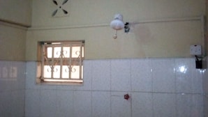 A bathroom with white tiled walls, a window with decorative bars, a ceiling fan, and a light fixture. - Olympia Hotel (Nyahururu)