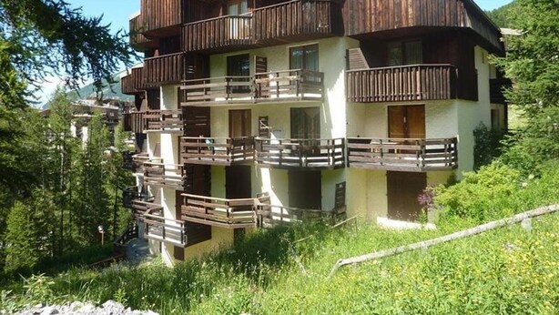A multi-story wooden chalet with balconies, surrounded by greenery and trees. - Studio 6 pers avec mezzanine, accès pistes, proche commerces, balcon Est (Les Orres)