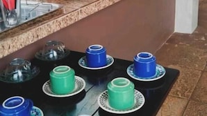 Un comptoir de cuisine sur lequel on trouve divers objets, notamment une machine à café, un mixeur et un panier de fruits. On y voit également plusieurs tasses et récipients.