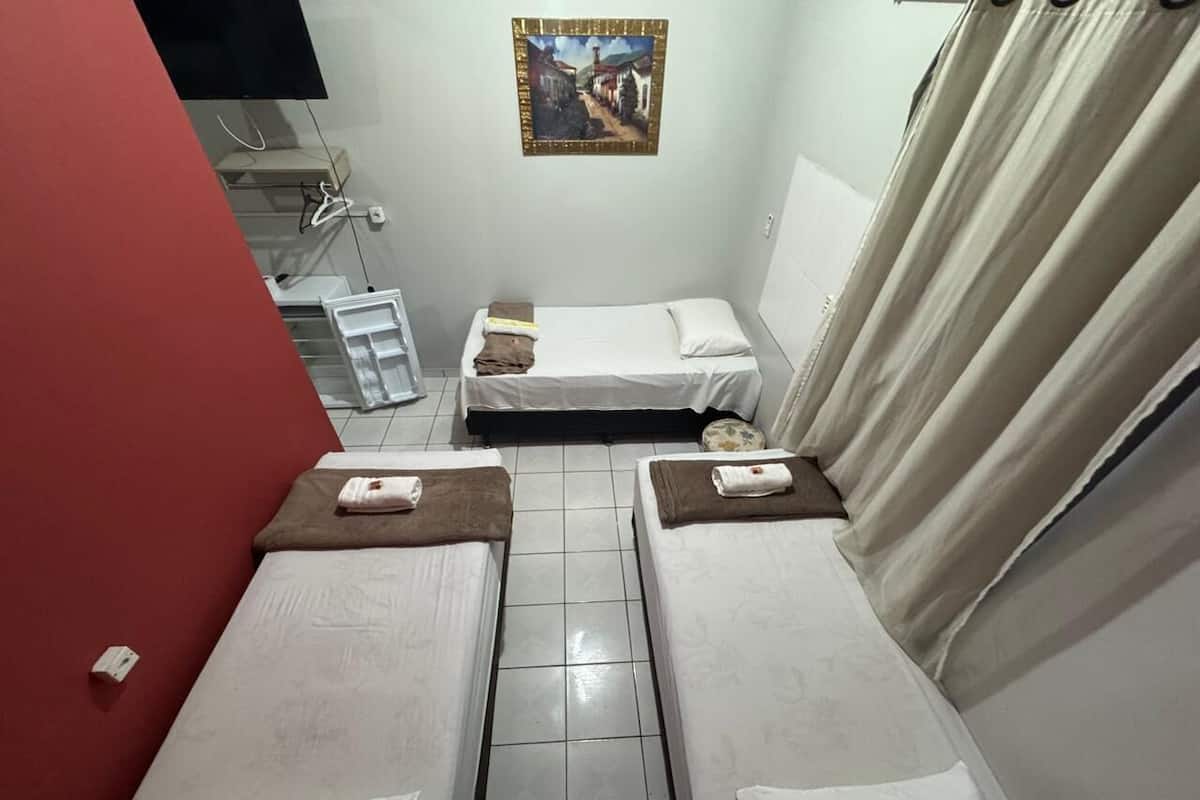 Une petite chambre compacte avec deux lits simples, une petite table et un téléviseur fixé au mur.
