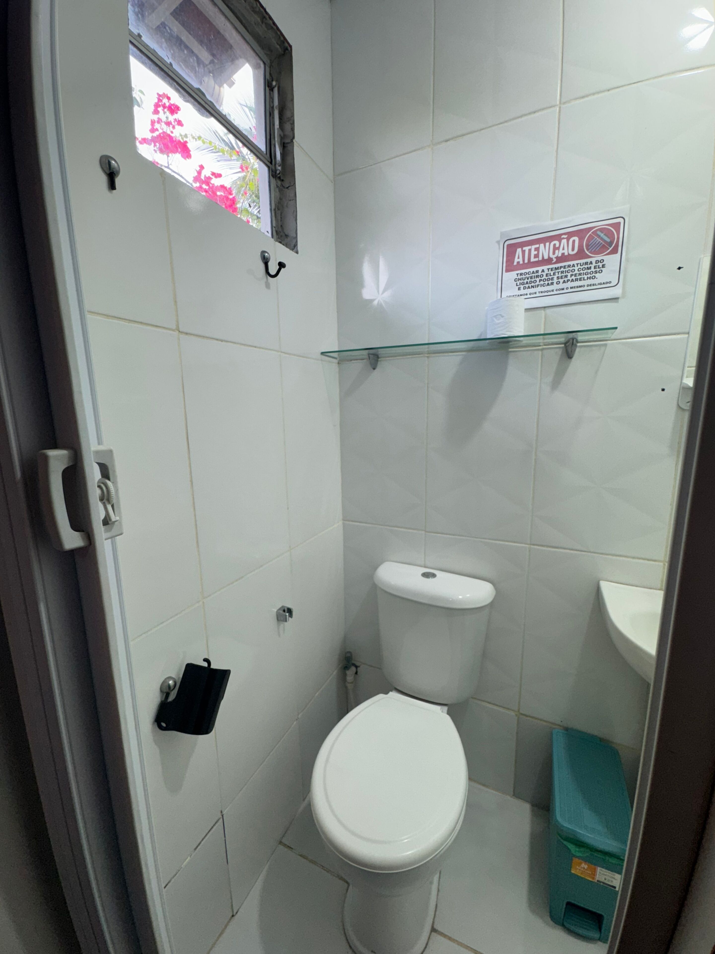 Un baño pequeño y blanco con un inodoro, una repisa de vidrio y un cubo de basura.
