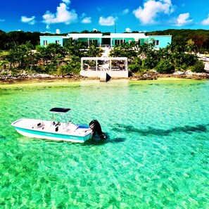 A boat anchored near a turquoise building with a clear view of the surrounding greenery and water. - ZION Beachfront | Luxury | ECO | Lagoon | Paddleboards | Snorkel | Volleyball (Governors Harbour)