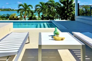 A poolside area with a table, chairs, and a view of the ocean.