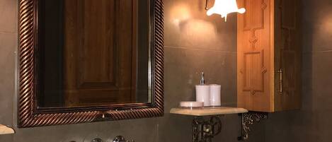 Un baño con un espejo grande, un lavamanos blanco, un gabinete de madera y una lámpara empotrada en la pared.