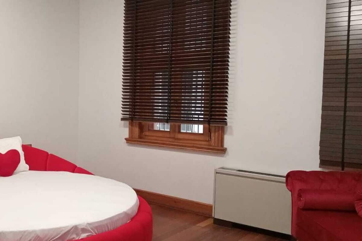 A bedroom with a round bed, a lion head decoration, a window with blinds, and a red chair.