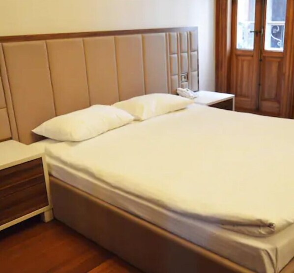 A neatly made bed with a wooden headboard, a bedside table with a phone, and a window with curtains. - Aslan Residence (Istanbul)