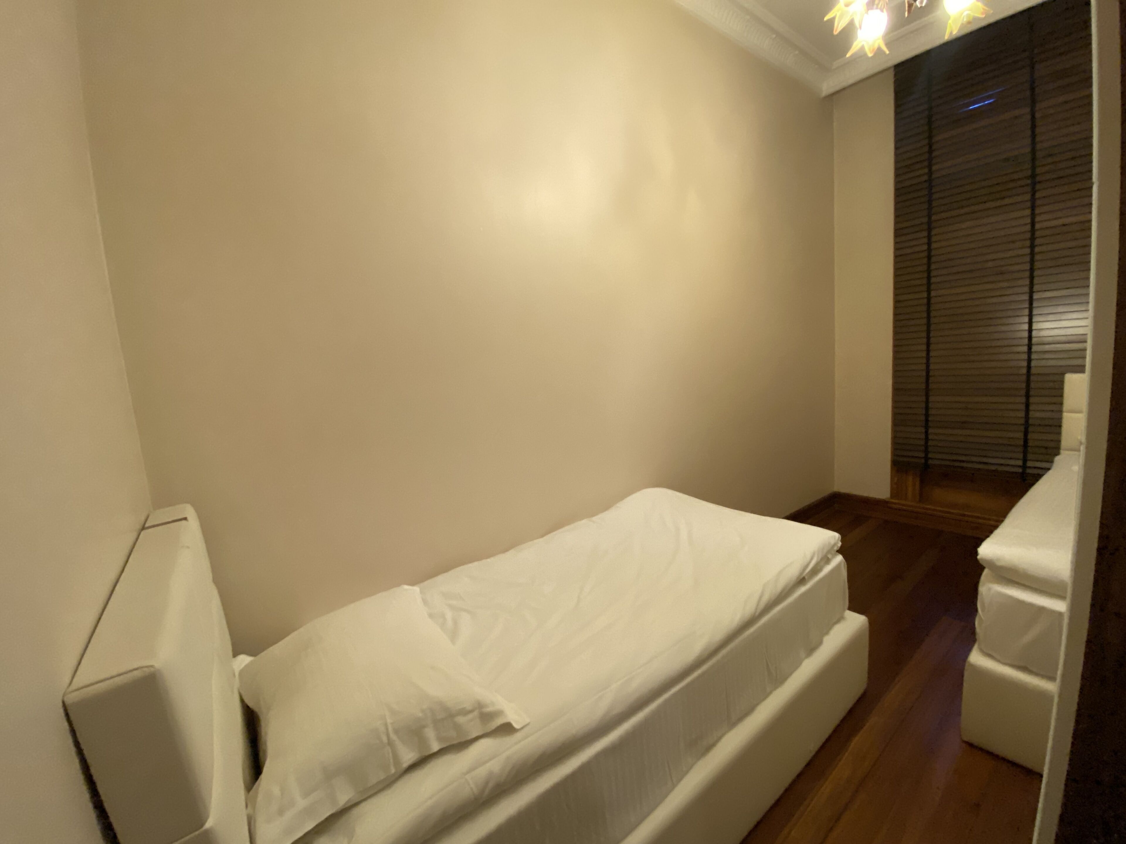 Ein kleines Zimmer mit einem Einzelbett, einer weißen Matratze, einem Nachttisch und Holzboden.