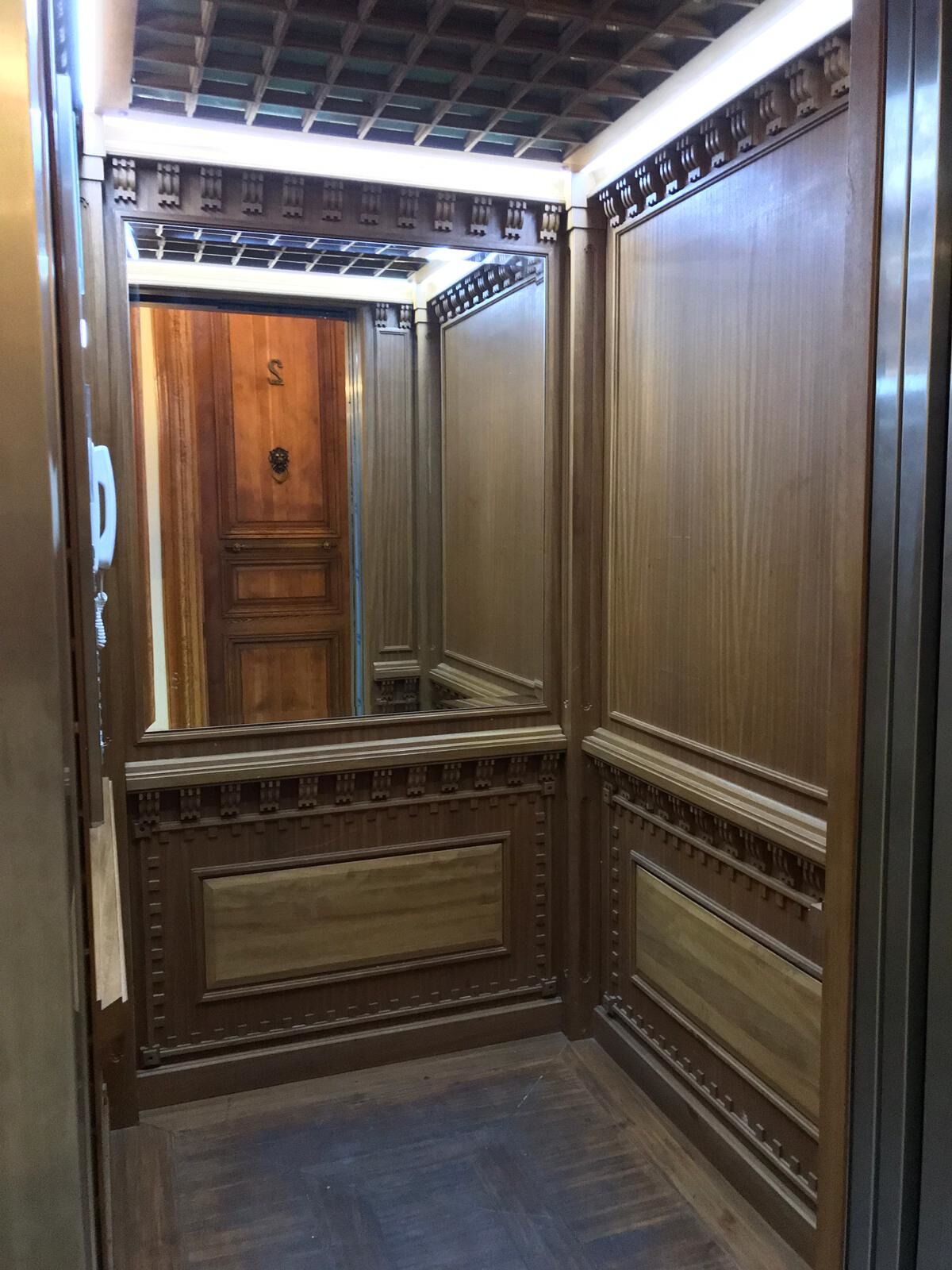 An elevator interior with wooden paneling and a mirrored wall.