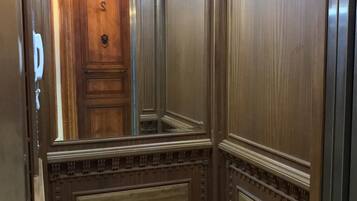 An elevator interior with wooden paneling and a mirrored wall.