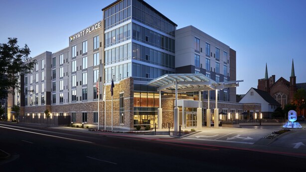 Een modern hotel met een glazen gevel, een overdekte ingang en een bord met de tekst 'HYATT PLACE'.