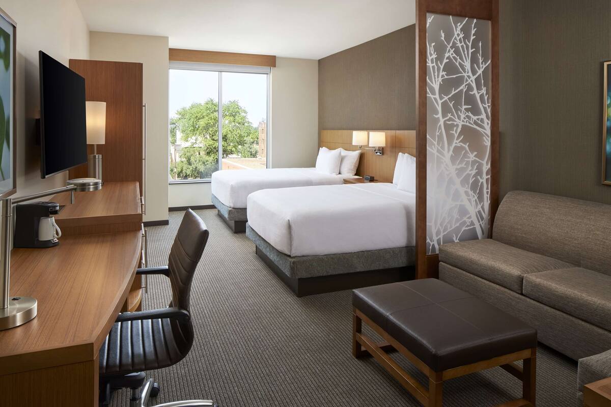 A hotel room with two beds, a desk with a chair, a sofa, and a TV.