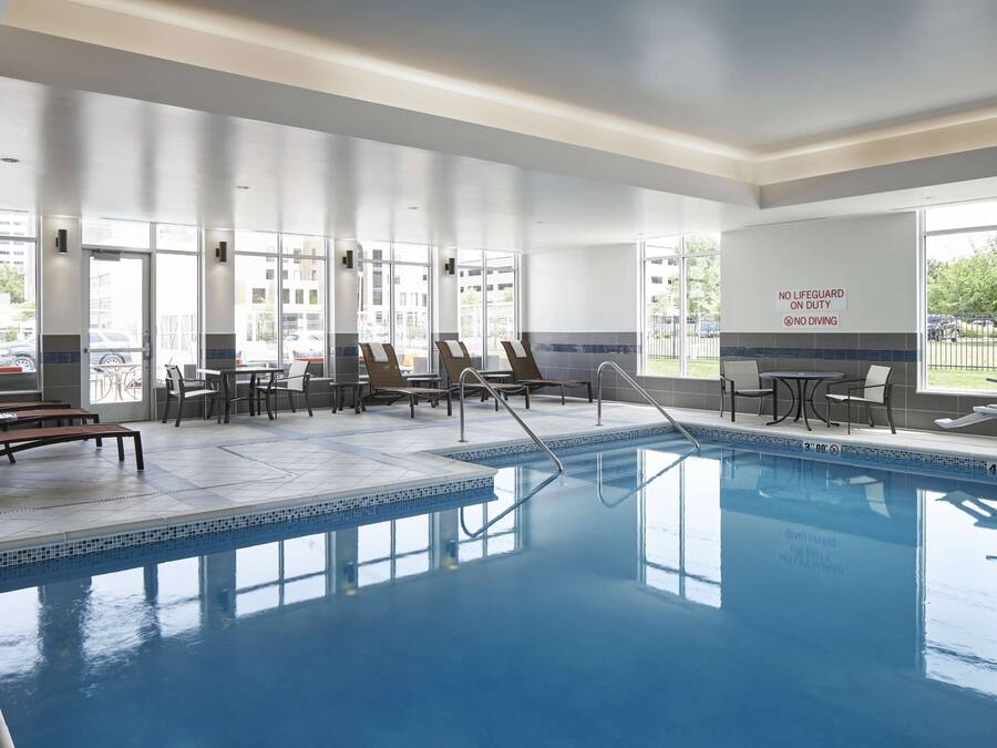 An indoor swimming pool with clear glass walls, lounge chairs, and a sign indicating no lifeguard on duty.