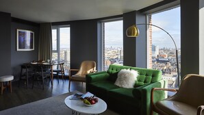A modern living room with a green sofa, a dining area, and a view of the cityscape through large windows. - The Gate London City (London)