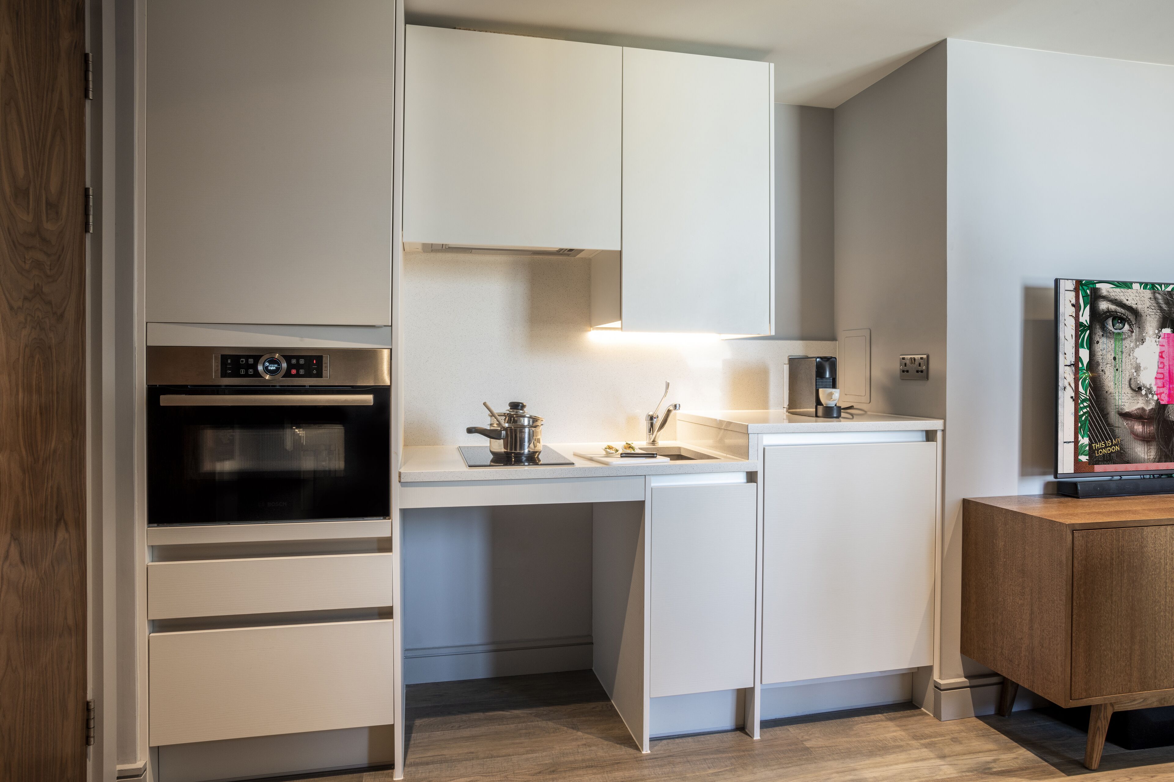 A modern kitchen with white cabinetry, a built-in oven, and a wooden cabinet with a television.