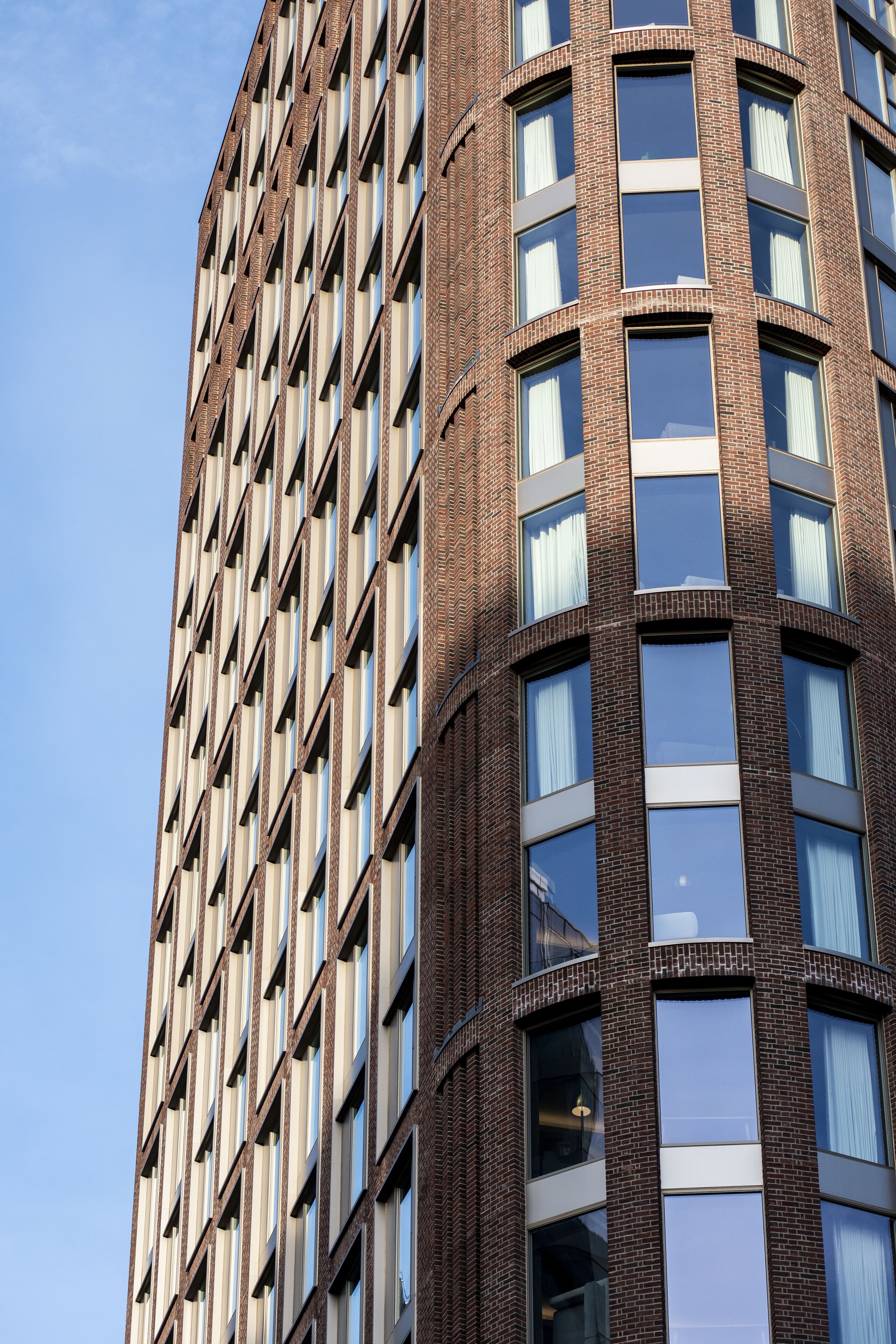 Un grand immeuble en briques, doté d’une façade à fenêtres disposées en réseau et d’un coin arrondi.