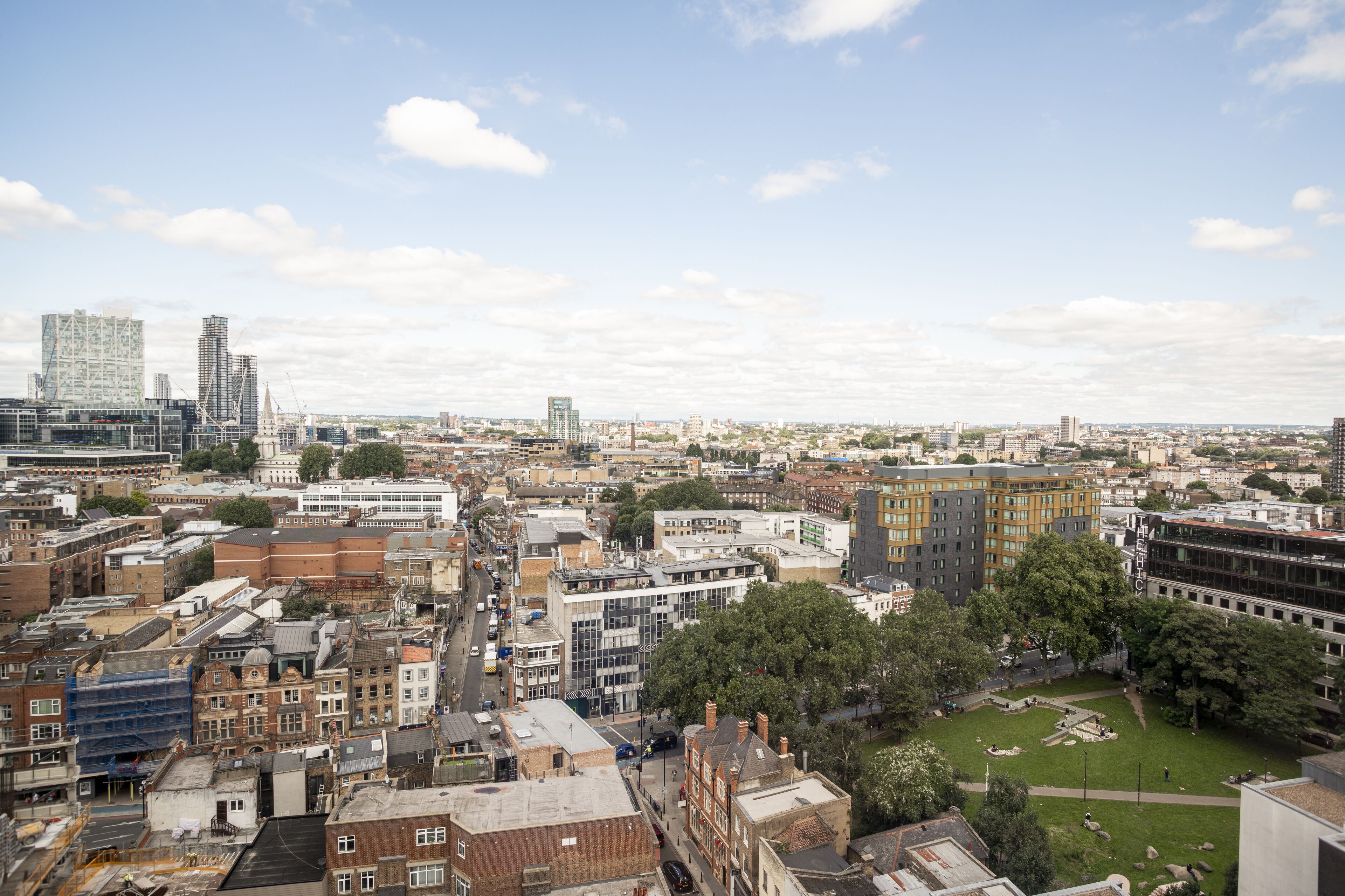 A cityscape with a mix of modern and older buildings, a central open square, and a clear sky.