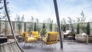 An outdoor patio area with wicker furniture, a hanging chair, and a wooden bench. - The Gate London City (London)