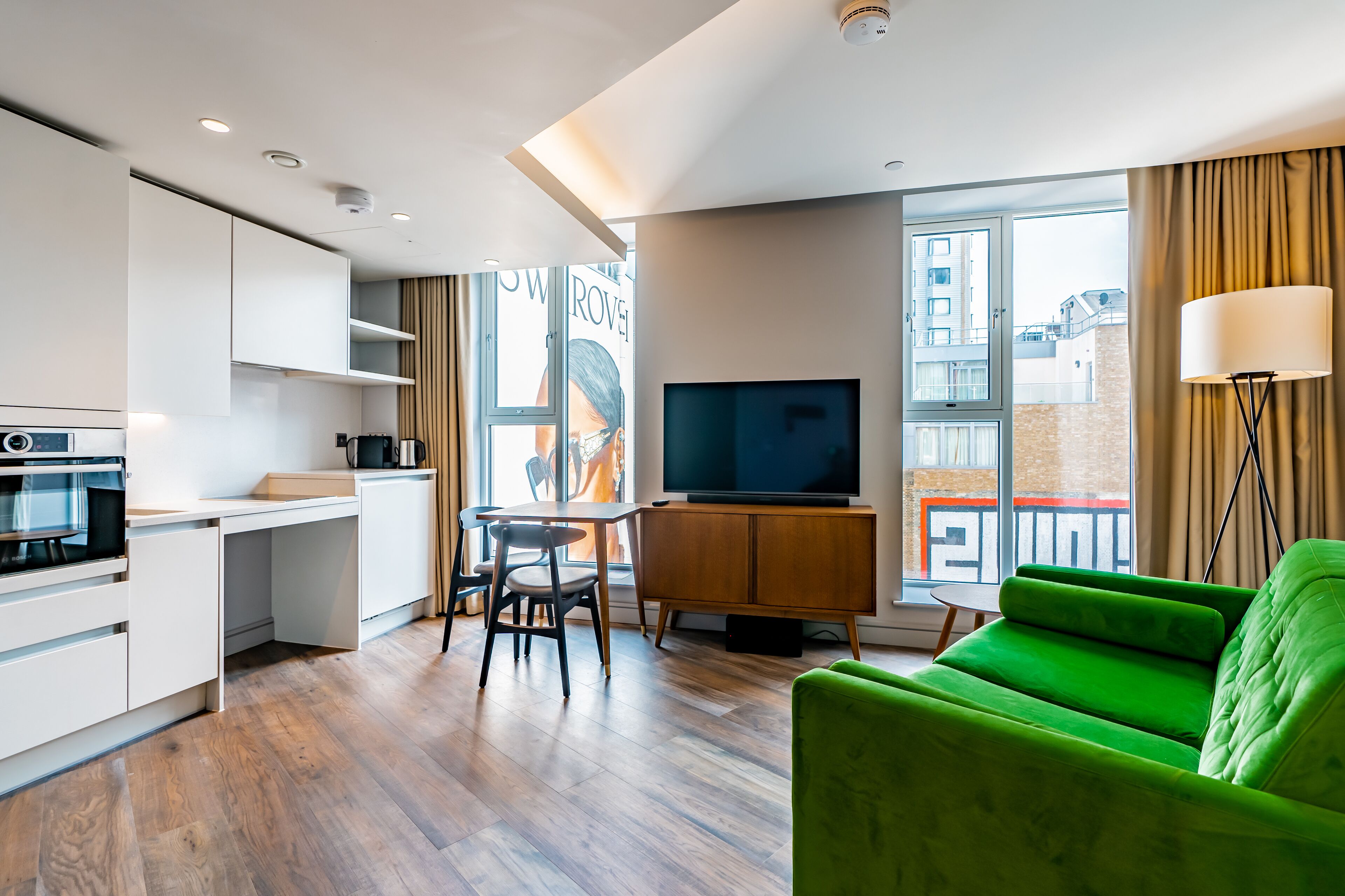 A modern living room with a green sofa, a TV, a dining area, and a kitchen.