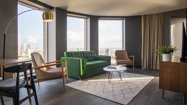 A modern living room with a green sofa, two chairs, a coffee table, and a large window offering a city view. - The Gate London City (London)