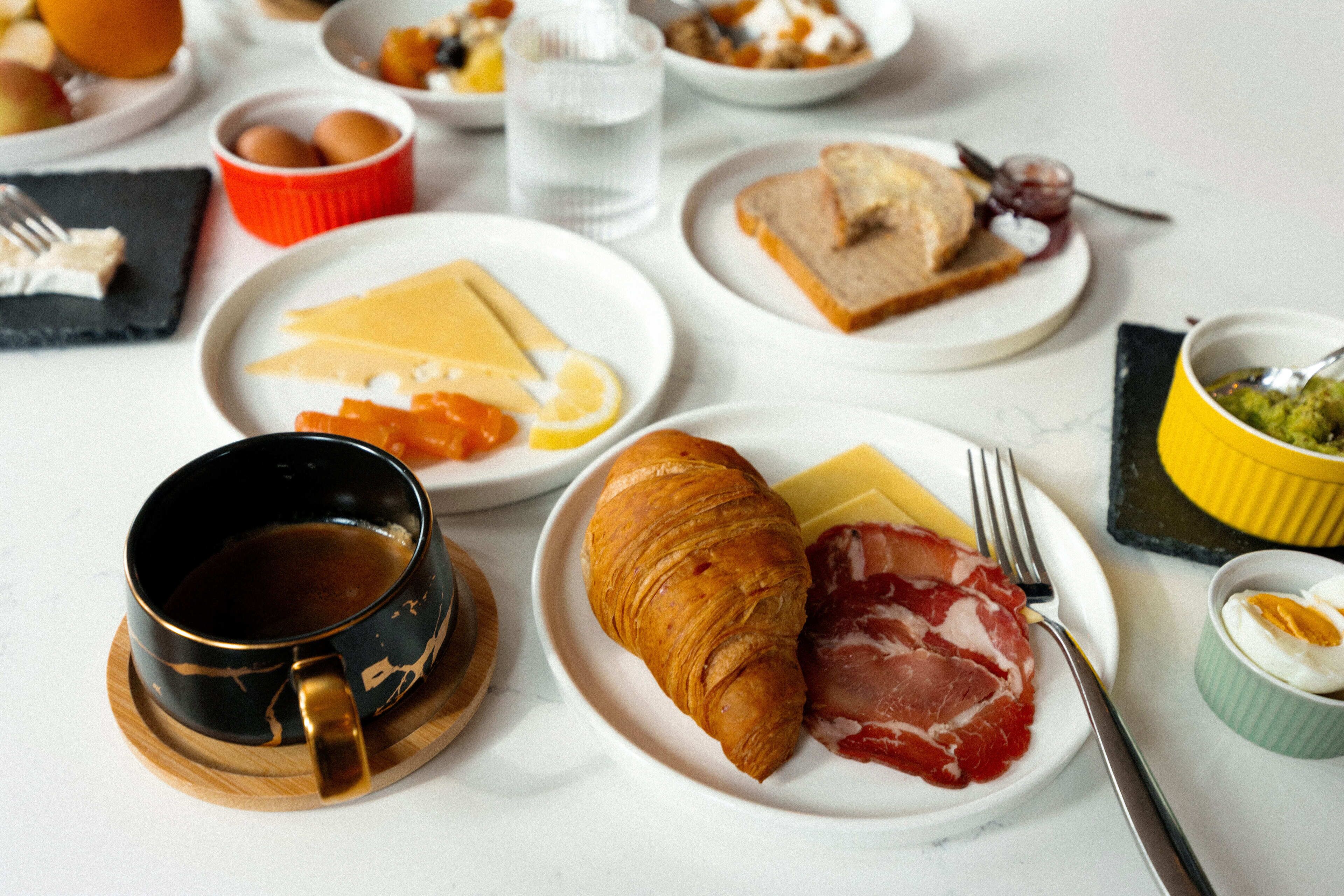 A breakfast setting with plates of food, including croissants, cheese, and ham, along with a cup of coffee.