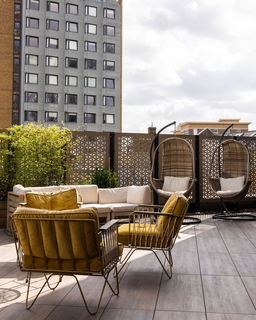 Terraza en la azotea con un sofá, dos sillones y una mecedora colgante.