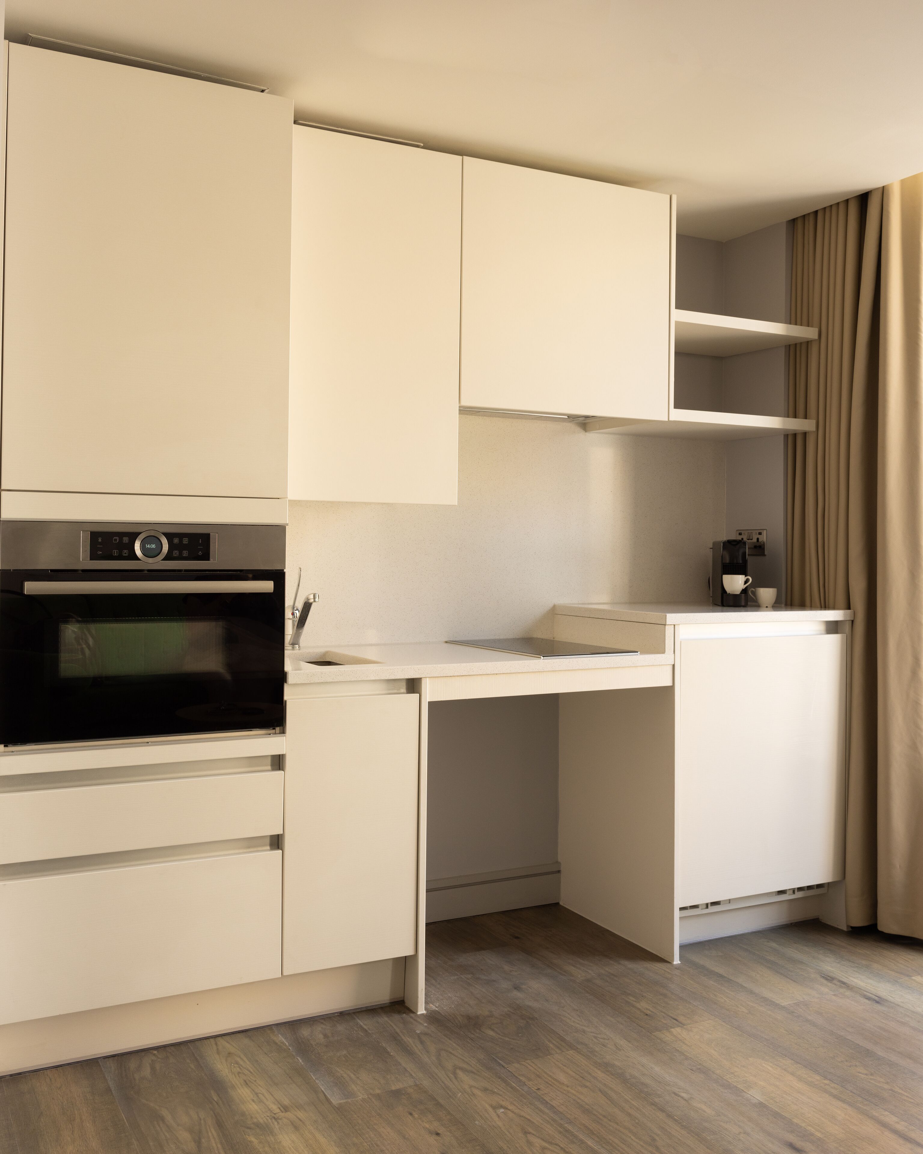 A compact kitchenette with a built-in oven, a coffee maker, and a small refrigerator.