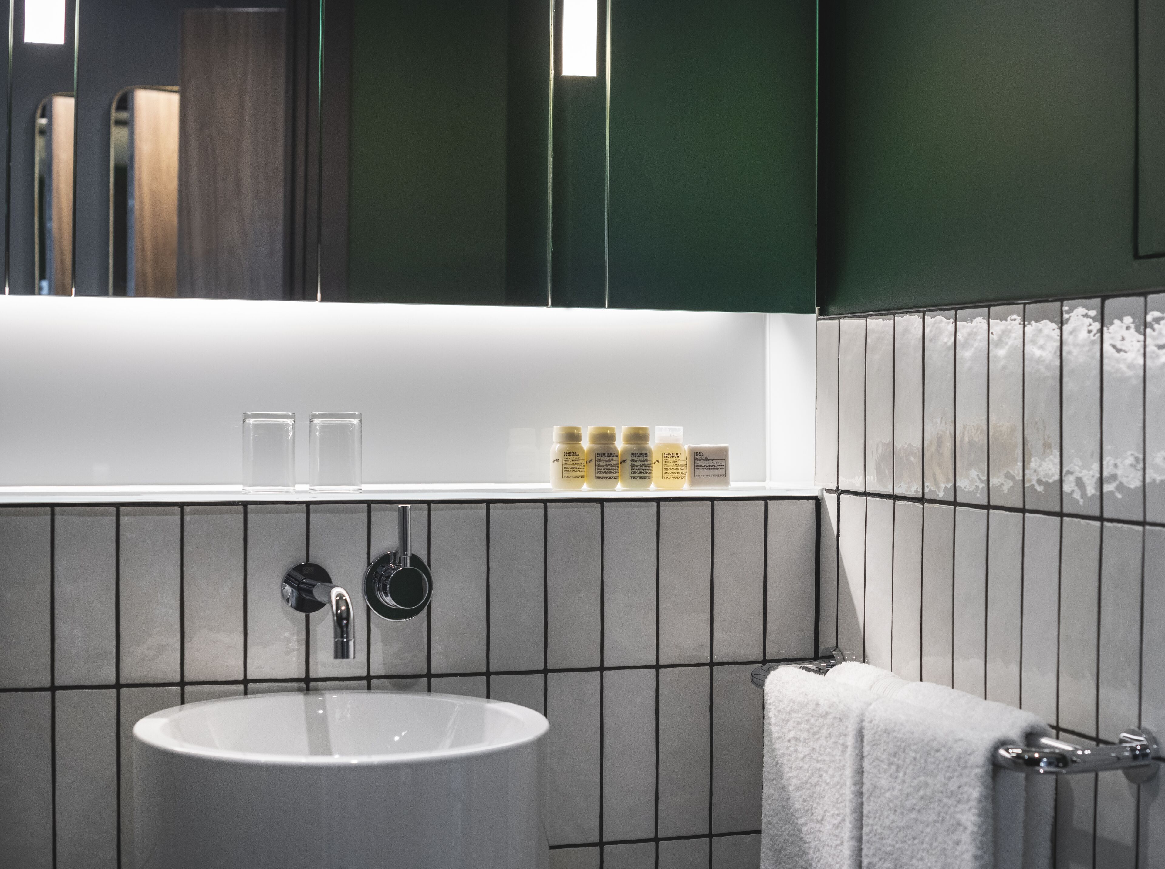 A modern bathroom with a white sink, dark green walls, and a tiled backsplash.